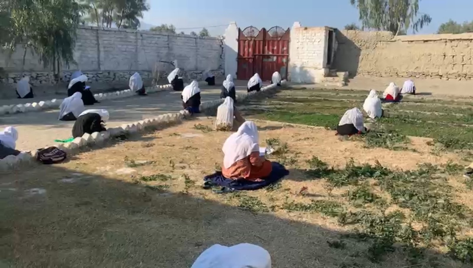 Students seated apart on the ground for an open-air class in a walled yard