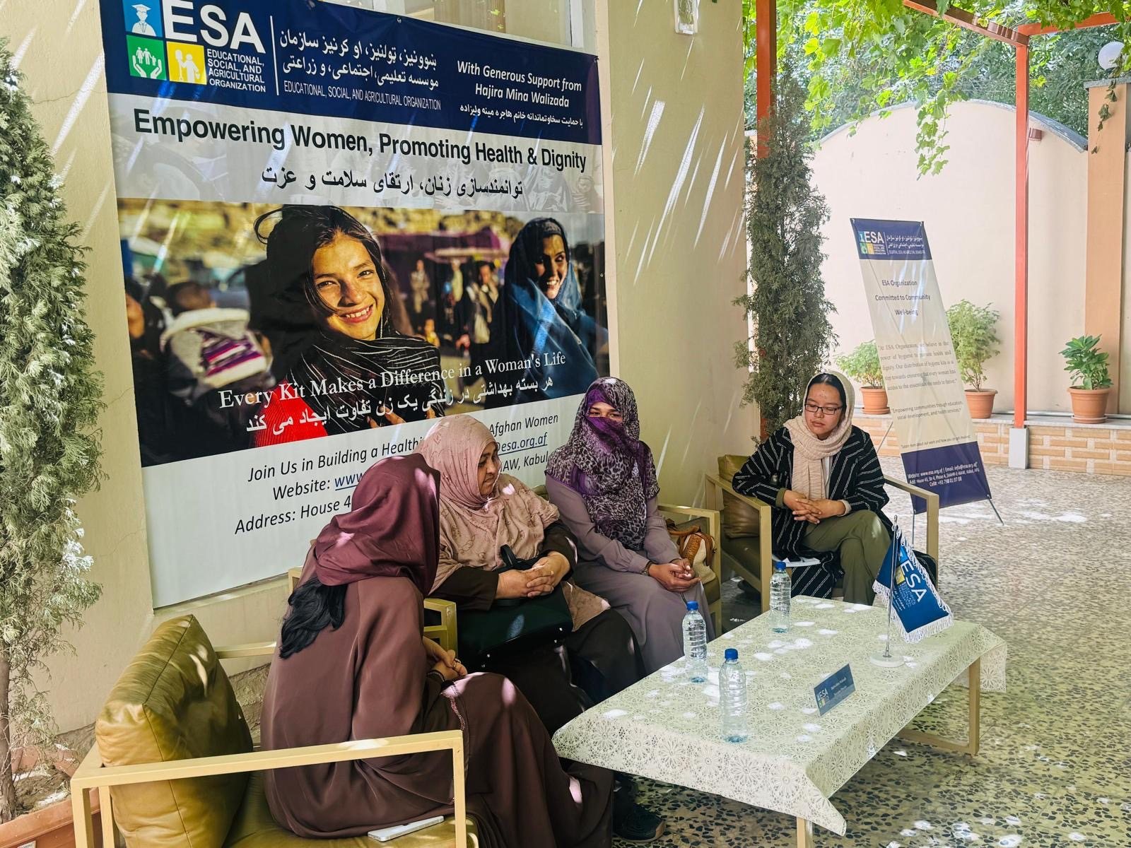 Community leaders and ESA staff seated together beneath a banner reading Empowering Women, Promoting Health and Dignity
