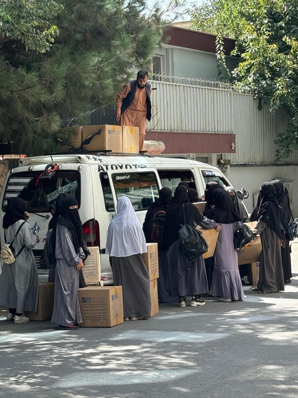 Women loading boxes of supplies onto a van, with more boxes being secured to the roof